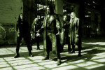 Vihertävä ja tumma valokuva Grabak-yhtyeen viidestä miesjäsenestä, jotka seisovat vaalealattiaisessa hallissa.