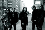 Kylmänsininen valokuva Shamrain-bändin viidestä miesjäsenestä, joista kaikki muut paitsi vasemmalla seisova ovat pukeutuneet mustiin vaatteisiin. Vasemmanpuoleisella miehellä yllään kulunut takki.