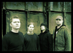 Nelimiehisen The Arcane Order -bändin jäsenet seisovat vihreäsävyisessä valokuvassa rautaisen seinän tai muurin edustalla. Osalla miehistä mustat paidat yllään, mutta oikeanpuoleisella hepulla vihreä maiharitakki ja lippis päässään.