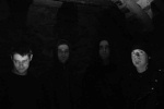 Mustavalkoinen ja erittäin tummasävyinen ryhmäpotretti For Ruin -bändin neljästä miehestä, jotka seisovat varjoissa. Heistä näkyy vain kasvot muuta taustaa vaaleampina.