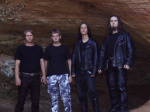 Nelihenkisen Urt-bändin miehet seisovat suuren kallioseinän tai tunnelin suuaukon edustalla rivissä. Kahdella oikeanpuoleisella miehellä mustat nahkavaatteet yllään, keskimmäisellä metrokuvioidut maastohousut, vasemmanpuoleisella mustat vaatteet.