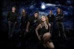 Tummasävyinen valokuva Visions Of Atlantis -bändin jäsenistä, joista viisi takana seisovaa on miehiä ja etummaisena vähäpukeinen henkilö on vaaleahiuksinen nainen. Taustalla paistaa Kuu ja tummansininen taivas.