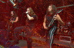 Punasävyinen valokuva Gory Blister -bändin joukoista, jotka ovat esiintymislavalla soittimet valmiina. Kuvassa kolme miestä, joista jokaisella pitkät hiukset. Keskimmäisellä mikrofoni suunsa edessä.