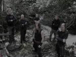 Hyvin tummasävyinen valokuva Cor Scorpii -yhtyeen joukosta, johon kuuluu kuusi miestä, joista lähes kaikilla pitkät hiukset. He ovat pukeutuneet mustiin vaatteisiin ja seisovat ulkoilmassa kivilouhikossa, jossa taka-alalla pensaita ja lehtimetsää.