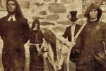 Verjnuarmu-yhtyeen miehet seisovat suurista kivistä muuratun seinän tai muurin edustalla vanhahtavassa kuvassa, jonka värimaailma ruskeaharmaa. Kuvassa viisi ihmishahmoa, joista vasemmanpuoleisella papin liperit kaulassa. Takana seisoo mies, jolla pitkät 