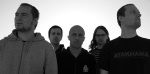 Mustavalkoinen valokuva Ghost Brigade -bändin kokoonpanosta, johon kuuluu viisi miestä. He seisovat vastavalossa vaaleata taustaa vasten. Laidoilla seisovat miehet katsovat vastakkaisiin suuntiin samalla kun kolme taka-alalla näkyvää miestä eteenpäin. Kes