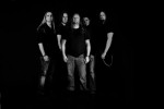 Mustavalkoinen ryhmävalokuva Thunderstone-bändin kokoonpanosta, johon kuuluu viisi mustiin pukeutunutta miestä. He seisovat tiiviinä rykelmänä pikimustassa ympäristössä.