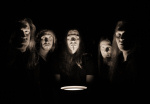 Mustanpuhuva ryhmäkuva Kalmah-yhtyeen miehistöstä, jonka jäsenten kasvot näkyvät mustaa taustaa vasten lampun valaistessa heidän kasvojaan. Miehistöä kuvassa viisi kappaletta. Jokaisella pitkät hiukset, osalla viikset, osalla partaa.