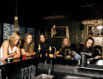 Children Of Bodomin jäsenet nojaavat laumana baaritiskiin, jonka päällä on pulloja ja laseja täynnä juomia. Kuvassa viisi miestä, joista oikeassa laidassa Alexi Laiho. Laiholla partaa ja viikset, pitkät hiukset.