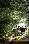 Jani Mahkosen ottama valokuva Entwinen kokoonpanosta. Bändin jäsenet seisovat rykelmänä vehreän luonnon helmassa. Kuvaa hallitsee vihreät lehtipuut. Miesten ympärillä hohkaa kullankeltaiset värivanat.