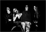 Mustavalkoinen valokuva Sauron-bändin miehistöstä, johon kuuluu raatomaskit naamalla irvisteleviä black metallisteja. Kuvassa neljä miestä, joista lähes kaikilla mustaa vaatetta yllään ja kasvoilla musta-valkoiset maalit. Yksi heppu laittaa pistoolia suuh