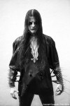 Harmaasävyinen valokuva Gorgoroth-bändin Infernus–nimisestä hahmosta, jolla pitkät hiukset ja raatomaskit naamalla. Miehellä yllään mustaa vaatetusta, käsivarsissa pitkät niittirannekkeet ja kaulassa ylösalaisin käännetty risti.