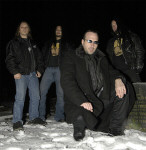 Mayhem-bändin jäsenet seisovat lumihangessa pakkasyönä. Etualalla Attila Csihar mustissa vaatteissa ja aurinkolasit silmillä.