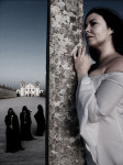 Valokuva Ava Inferi -nimisen metallibändin kokoonpanosta. Etualalalla seisoo valkoiseen kaapuun pukeutunut mustahiuksinen nainen, joka katsoo vakavanoloisesti pylvääseen nojaten eteenpäin. Hänen takanaan voimakkaansininen taivas ja kolme mustiin kaapuihin