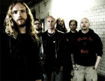 Dark Tranquillity -bändin promokuva, jossa miehet seisovat vaaleata tiiliseinää vasteen. Kuvassa kuusi miestä, joista yksi on kalju.