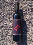 Samaelin logolla varustettu musta viinipullo lojuu avaamattomana hienojyväisessä hiekassa.