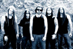 Construcdead-bändin jäsenet sinisävyisessä kuvassa. Miehet seisovat kiviseinän tai -kasan edessä. Miehillä on yllään mustat paidat, joissa ei ole hihoja. Keulahahmolla on partaa ja mustat aurinkolasit silmillään.