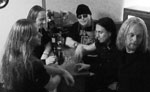 Harmaasävyinen ryhmäkuva Dauntless-yhtyeen kokoonpanoon kuuluvista viidestä miehestä. He istuvat pöydän äärellä. Kuvan jäsenistä lähes kaikilla mustaa vaatetta päällä ja pitkät hiukset päässä.