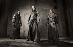 Valokuva kolmesta mustiin pukeutuneesta Behemoth-bändin jäsenestä, jotka seisovat rivissä harmaasävyisessä valokuvassa. Keskimmäisenä on Nergal. Jäsenillä pitkät hiukset, nahkavatteet ja corpsemaskit kasvoilla.