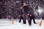 Project: Metal Nationin kolme ydinjäsentä seisoo lumihangessa keskellä kuusimetsää. Kuvassa näkyvillä miehillä mustat vaatteet ja yhdellä musta lippu kädessä. Maassa palaa pari jätkänkynttilää.
