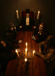 Verjnuarmun kokoonpanosta otettu synkkä valokuva, jossa muusikot istuvat pitkän puupöydän äärellä kynttilävalaistuksessa.