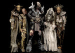 Ryhmäkuva hirviöasusteisiin pukeutuneesta Lordi-bändistä. Bändin jäsenet seisovat pikimustaa taustaa vasten. Keskimmäisenä on Mr. Lordi.