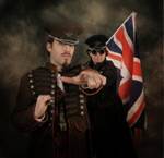 Valokuva kahdesta Imperial Vengeancen jäsenestä, joista molemmat ovat miehiä. Heillä on koppalakit päässä ja vanhanaikaiset uniformut yllään. Oikeanpuoleinen mies pitää Britannian lippua olalla.