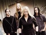 Ryhmäkuva Izegrim-bändistä, jonka keulahahmona on vaaleahiuksinen nainen, joka katselee tyynesti eteensä mustiin vaatteisiin puettuna.