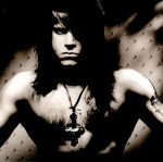Danzig-bändin keulahahmo ylivalottuneessa ja lähes mustavalkoisessa valokuvassa. Miehellä ei ole paitaa yllään, hänellä on puolipitkät hiukset ja kaulassa suurehko kaulakoru.