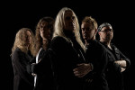 Saxon-bändin jäsenet seisovat mustaa taustaa vasten yhdessä ryppäässä. Miehiä kuvassa viisi kappaletta, joista jokainen on ohittanut keski-iän.