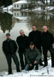 Demigod-bändin jäsenet seisovat joen rannassa. Rannassa vielä valkoista lunta maassa. Miehet, joita kuvassa viisi kappaletta, seisovat yhtä lukuunottamatta vieretysten. Etualalla istuu lippalakkipäinen keulahahmo.