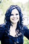 Kuvassa Nightwishin entinen vokalisti, Anette Olzon, jolla musta kurvikas tukka ja hymyilevä ilme kasvoilla.