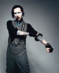 Marilyn Mansonin Brian Warner seisoo maskit kasvoilla ja kummalliset harmahtavat puvun vaatteet yllään. Mies ojentelee käsiään. Käsivarsissa tatuointeja.