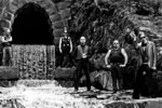 Harmaasävyinen ryhmäkuva Church of Void -bändin jäsenistä. Miehet seisovat ulkoilmassa vanhan kivimuurin edustalla.