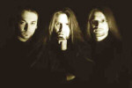Kolmihenkisen Dark At Dawn -yhtyeen jäsenet seisovat tummasävyisessä valokuvassa. Kahdella miehistä pitkä vaaleahkot hiukset, vasemmanpuoleisella lyhyt musta tukka. Miehillä yllään musta vaatetus.