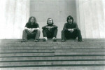Mustavalkoinen bändikuva kolmihenkisestä Requiem Aeternam -yhtyeestä, jonka jäsenet istuvat rivissä kiviportaiden yläpäässä. Taustalla kaksi suurta vaaleaa kivipylvästä.