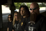 Slayer-bändin neljä jäsentä seisoo rivissä jonkinlaisen katoksen alla. Ulkona on kesäinen sää. Katoksen alla varjoisaa. Oikeassa laidassa mies, jolla pitkä pujoparta. Hänellä silmien edessä aurinkolasit.