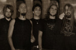 Viisihenkisen Max Midsun -yhtyeen jäsenet seisovat rivissä hyvin tummasävyisessä valokuvassa. Miehillä yllään mustat vaatteet. Osalla heistä pitkät hiukset tai muuten vaan runsaasti karvoitusta.