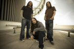 Korn-bändin kolme jäsentä kadulla. Keskimmäinen kyyristelee kahden hänen takanaan seisovan edessä. Miehillä arkivaatteet yllään. Heillä pitkät hiukset, kahdella taaimmaisella rastat.