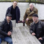 Neljä valkoihoista Sieges Seven -bändin jäsentä istuu ja seisoo puisen ja maalaamattoman pöydän edessä. Kaksi etummaista istuu, taaemmat seisovat. takana on merta, joka laineilee. Miehillä arkivaatteet yllään.
