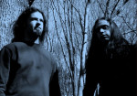 Sickening Horror -bändin kaksi miespuolista jäsentä seisoo keskellä puumetsää sinisävyisessä valokuvassa. Miehillä pitkät hiukset. Kuvakulma alhaalta ylöspäin, joten miehet näyttävät suurilta.