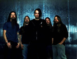 Lamb Of God -nimisen bändin neljä mustanpuhuvaa mieshahmoa seisoo rivissä suurta osittain valaistua merensinistä seinää vasten. Etualalla mustiin pukeutunut mies, jolla puolipitkät mustat hiukset ja kasvoilla parin päivän sänki.