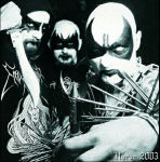 Mustavalkoinen valokuva Naer Mataron -yhtyeen kolmepäisestä black metal –joukkueesta, jolla on maskit kasvoilla ja bändipaitoja sekä niittirannekkeita yllään. Vasemmassa laidassa näkyvällä hepulla kädessään iso puukko.