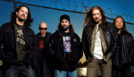 Viisi Dream Theater -nimisen bändin jäsentä seisoo rivissä tummansinistä taivasta vasten. Kuvan yläosassa ja miesten takana näkyy verkkoaitaa, jonka harjalla piikkilankaa.
