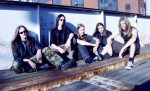 Viisi Amoral-bändin jäsentä istuu kesäisessä ulkoilmassa jonkinlaisessa junaradalla, jonka laidalla kulkee matalahko metalliaita.
