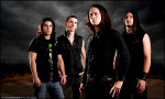 Tummasävyinen valokuva Trivium-bändin jäsenistä, joita kuvassa neljä kappaletta. Miehet seisovat mustiin tai tummiin vaatteisiin pukeutuneena synkän myrskytaivaan alla.