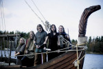 Ensiferumin jäsenet seisovat viikinkialuksen keulassa pukeutuneena viikinkiaiheisiin vaatteisiin. He ovat myös maalanneet kasvoihinsa mustia viivoja. Vene on vesillä, puuraja taustalla.