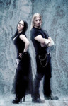Kaksi Tacere-bändin keulahahmoa seisovat mustiin pukeutuneina kylmänsinistä taustaa vasten. Kuvassa vasemmalla nainen, jonka vierellä seisoo mies. Naisella pitkät mustat hiukset, miehellä taas vaaleat.