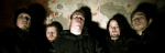 Viisi mustiin pukeutunutta Deadsoil-bändin jäsentä seisoo rähjäistä seinää vasten valokuvassa, jossa varjot ovat nielleet pimeyteen kuvan alaosan ja reunat.