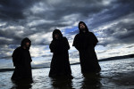 Kolme mustiin kaapuihin pukeutunutta Ulver-yhtyeen jäsentä seisoo polviaan myöten syvänsinisessä merivedessä. Taustalla uhkaavia, tummia ja jylhiä pilviä horisonttiin asti. Miesten takana, kaukana, näkyy mustana puurajaa.